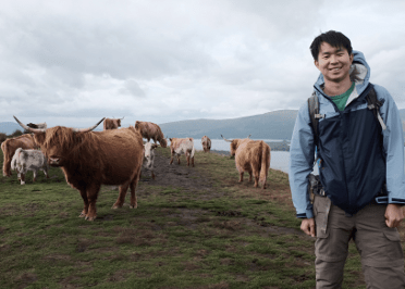 A walker poses gleefully with a group of shaggy highland cows.