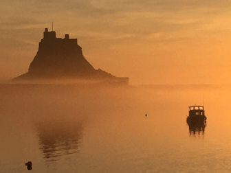 Holy Island stands from still waters, everything orange in the sunlight.