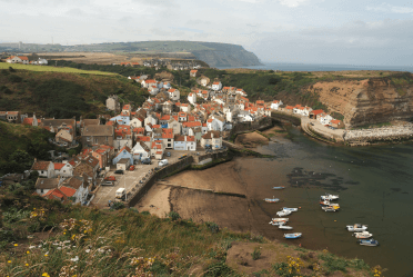 An aerial view of Staithes, a red-roofed harbour town, from the cliffs that overlook it on the Cleveland Way.