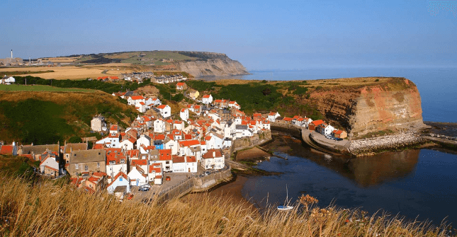 Pretty white houses with red rooftops cluster beside a bay on the Cleveland Way.