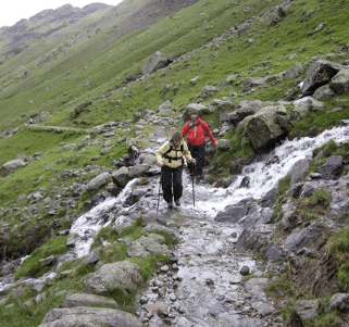 Friends walking together struggle across a flooded bit of rocky path.