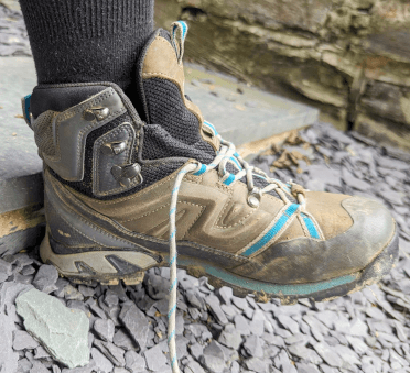 A walker seats their foot firmly in their boot by tapping the heel against a stone step.