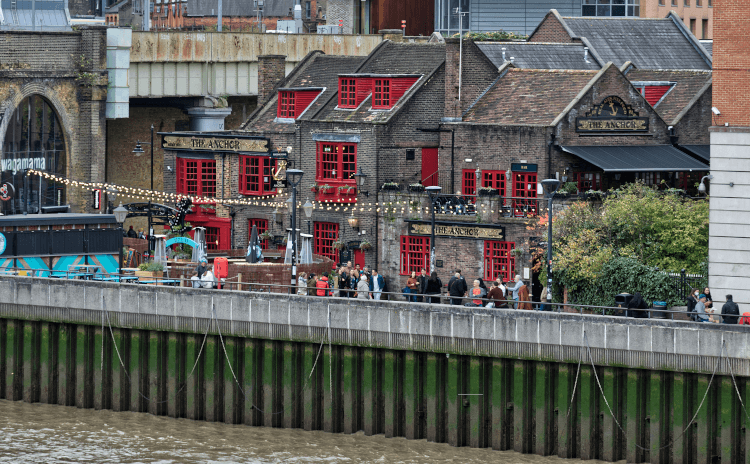 Riverside pub by Geoff Henson. The Anchor sits on the shore of the River Thames, with outdoor seating and large windows with their old wooden frames painted red.
