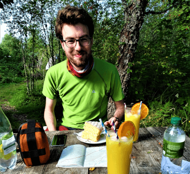 A walker sits at an outdoor table with a mug of tea, glass of orange juice, and the all-important fuel for a multi-day walk: cake.