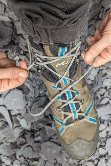 The hiker has started to lace her boots in reverse. From the top hooks, she has crossed her laces over and secured them around the pair of hooks that are second from the top.