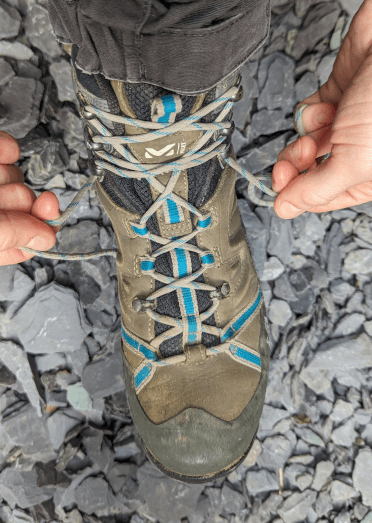 The hiker has criss-crossed her laces all the way down to the bottom pair of hooks and pulls the lace snugly.