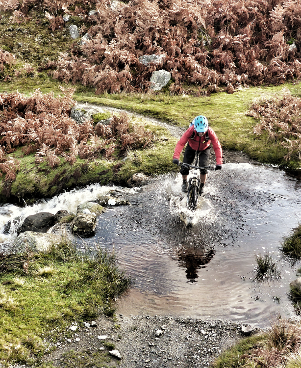 Mountain biker splashes through an overflowing river on the Trans Cambrian Way