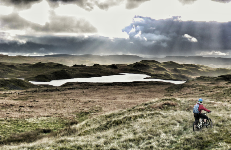 Dramatic lighting streams down over the wilderness and a distant lake on the Trans Cambrian Way