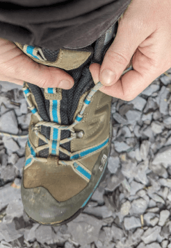 A walker laces her boots vertically from one eyelet to the one immediately above it to create gap lacing, a useful lacing trick for long-distance walking holidays.