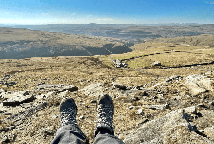 Views over green Yorkshire and a neighbouring farmhouse from atop Great Whernside, where our author sits with hiking booted feet outstretched.