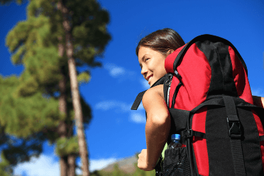 Wearing a backpack, a walker smiles over her shoulder as she explores the countryside.