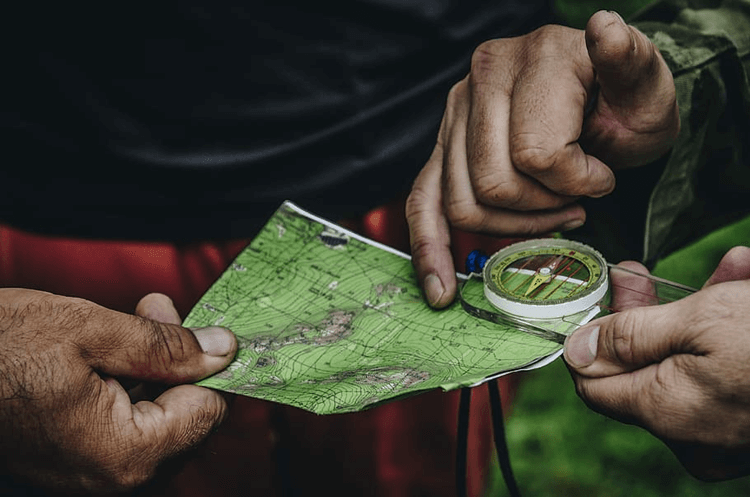 A close-up photo of hikers holding essential walking equipment, a map and compass, and pointing out the landmarks that will help them navigate.