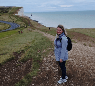 Gosia stands on a trail leading along the edge of the white cliffs, with the lighthouse at Beachy Head in the background.