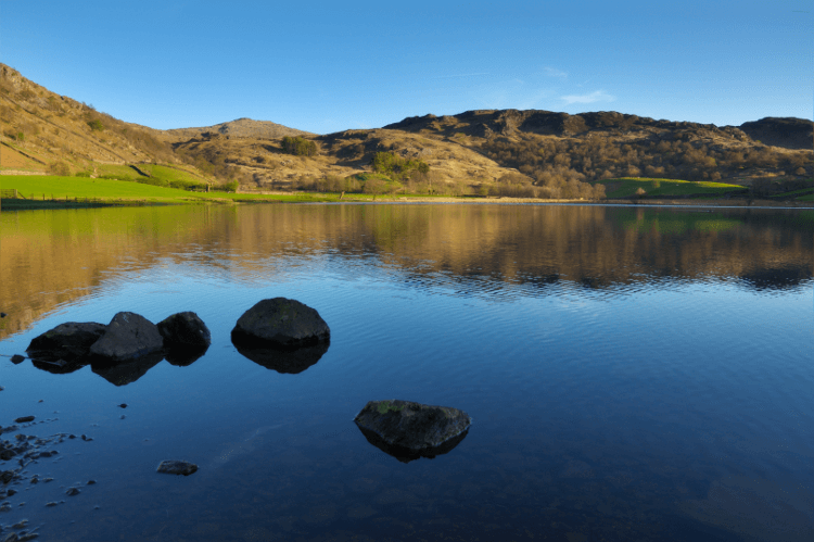 The blue water of Watendlath Tarn stands almost perfectly still beneath Lake District Fells on the Old Tourist Route.