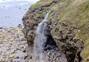 Rainwater gushes over craggy coastal cliffs and down to the sea.