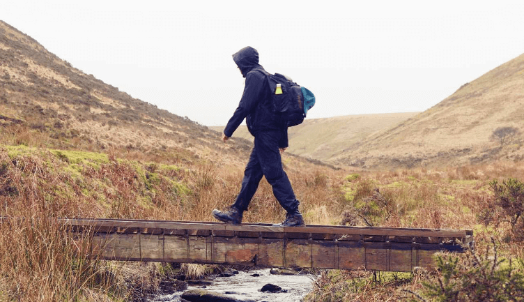 A hiker crosses a bridge on the Tarka Trail, fully kitted up in waterproof jacket, trousers and boots.