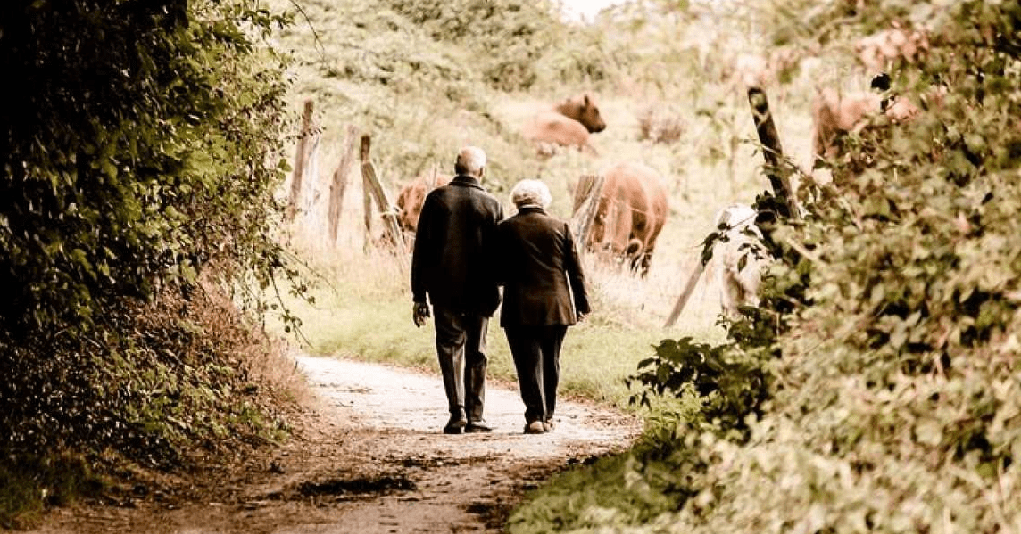 An older couple walk along a path toward a field of cows, an example of the gentle exercise that can help with diabetes.
