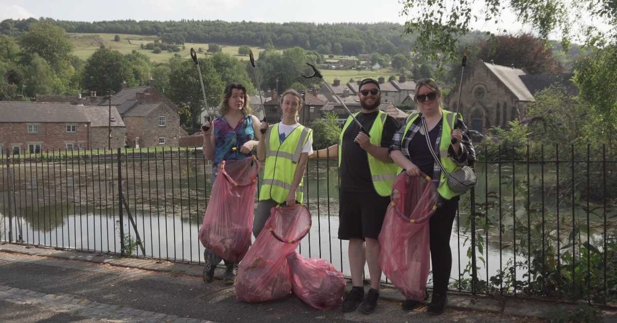 The Contours Holidays litter picking team stand with their litter-pickers in front of the pond in Cromford.