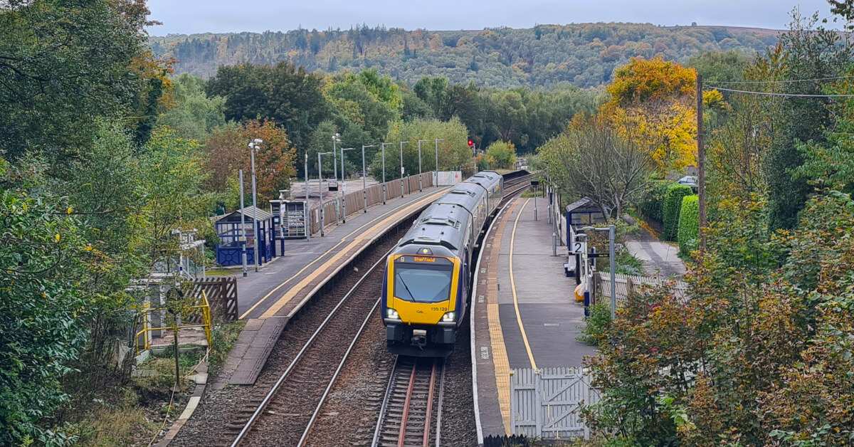 A train sits at a tiny local station in rural England, not far from a walking trail.
