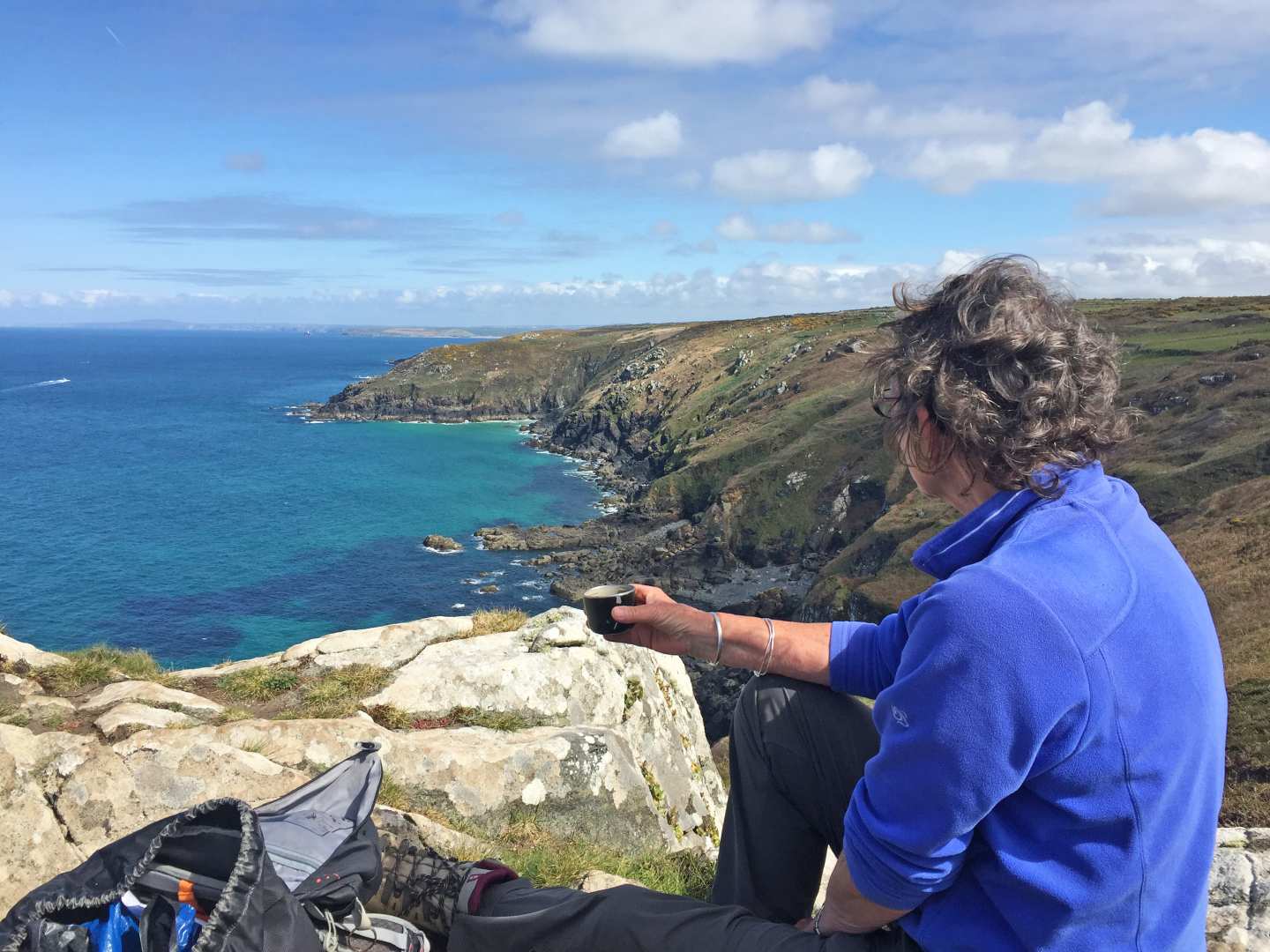 A walker sits on the Cornish coast with a cup of tea